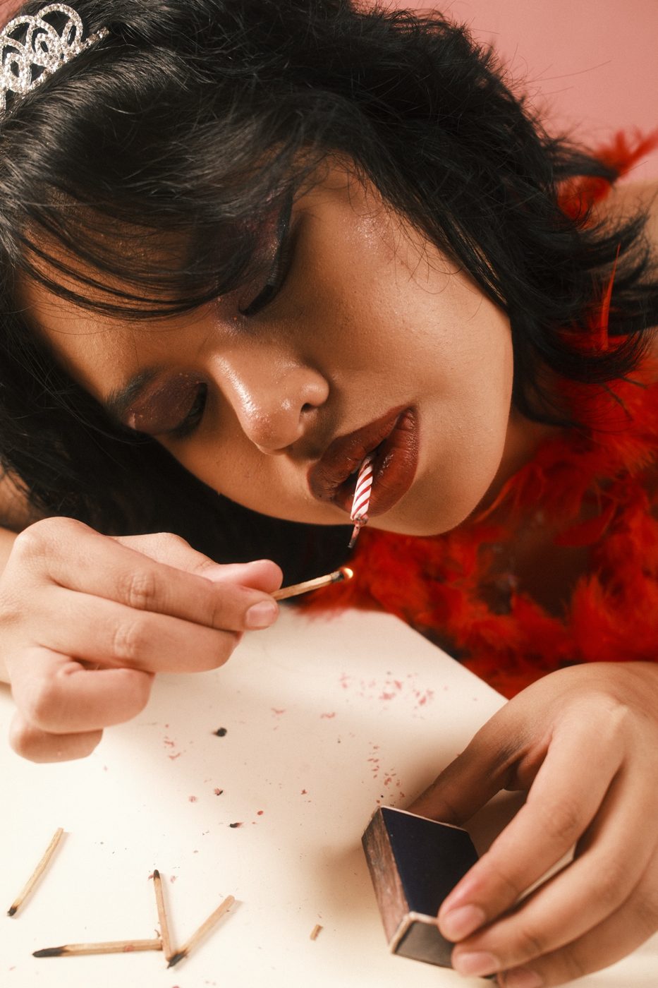 Head down on a table, a birthday candle between her lips, lighting a match among burnt ones