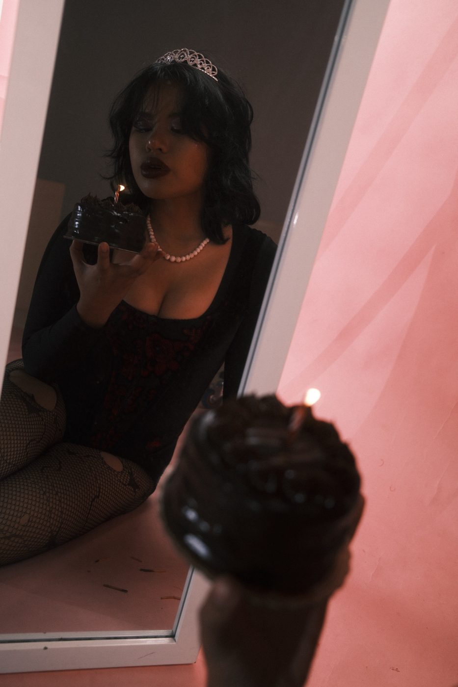 Her reflection in a mirror blowing out a candle, a second lit cake blurred in front