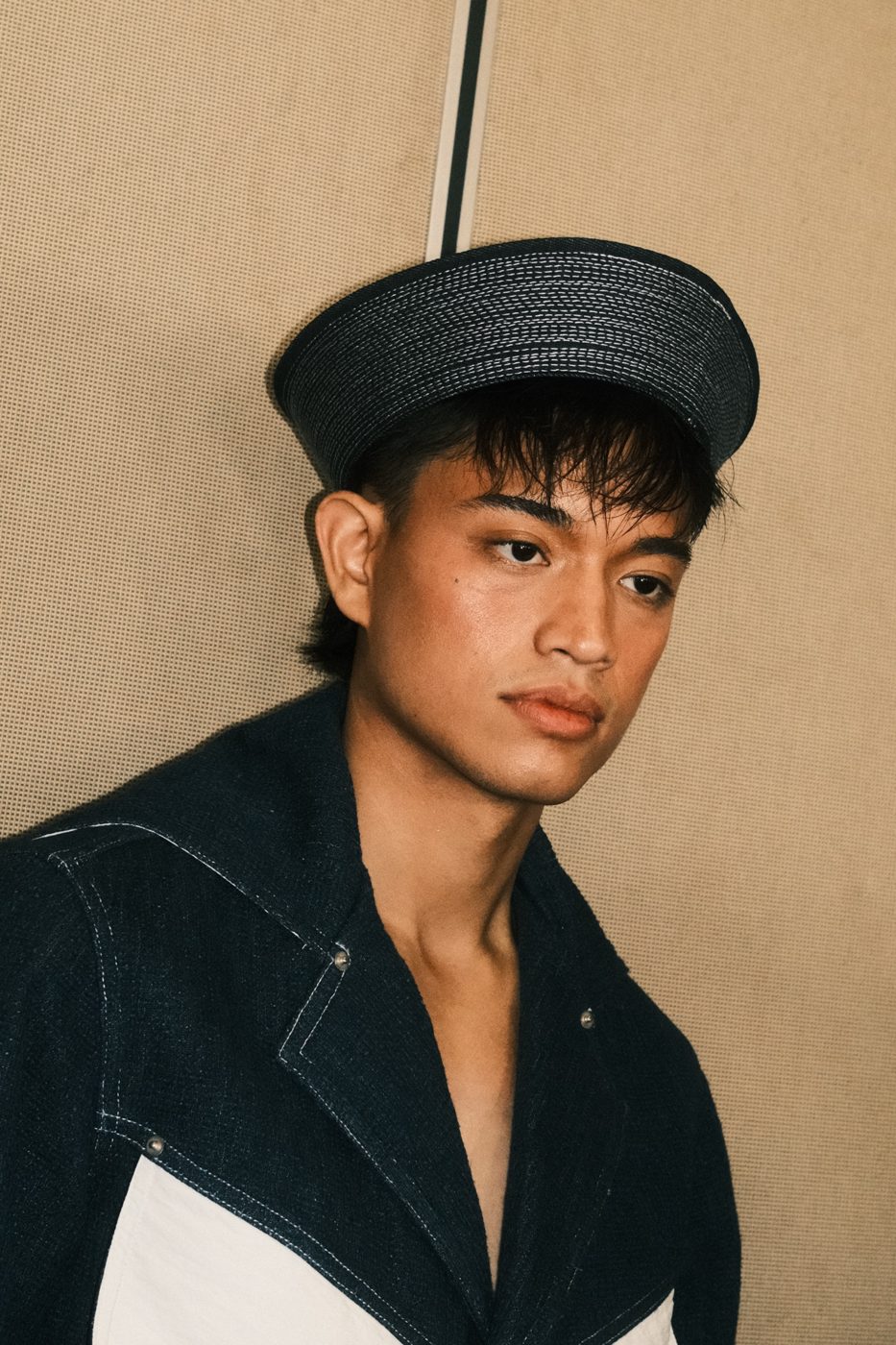 Model in a denim sailor hat and collar against a woven backdrop
