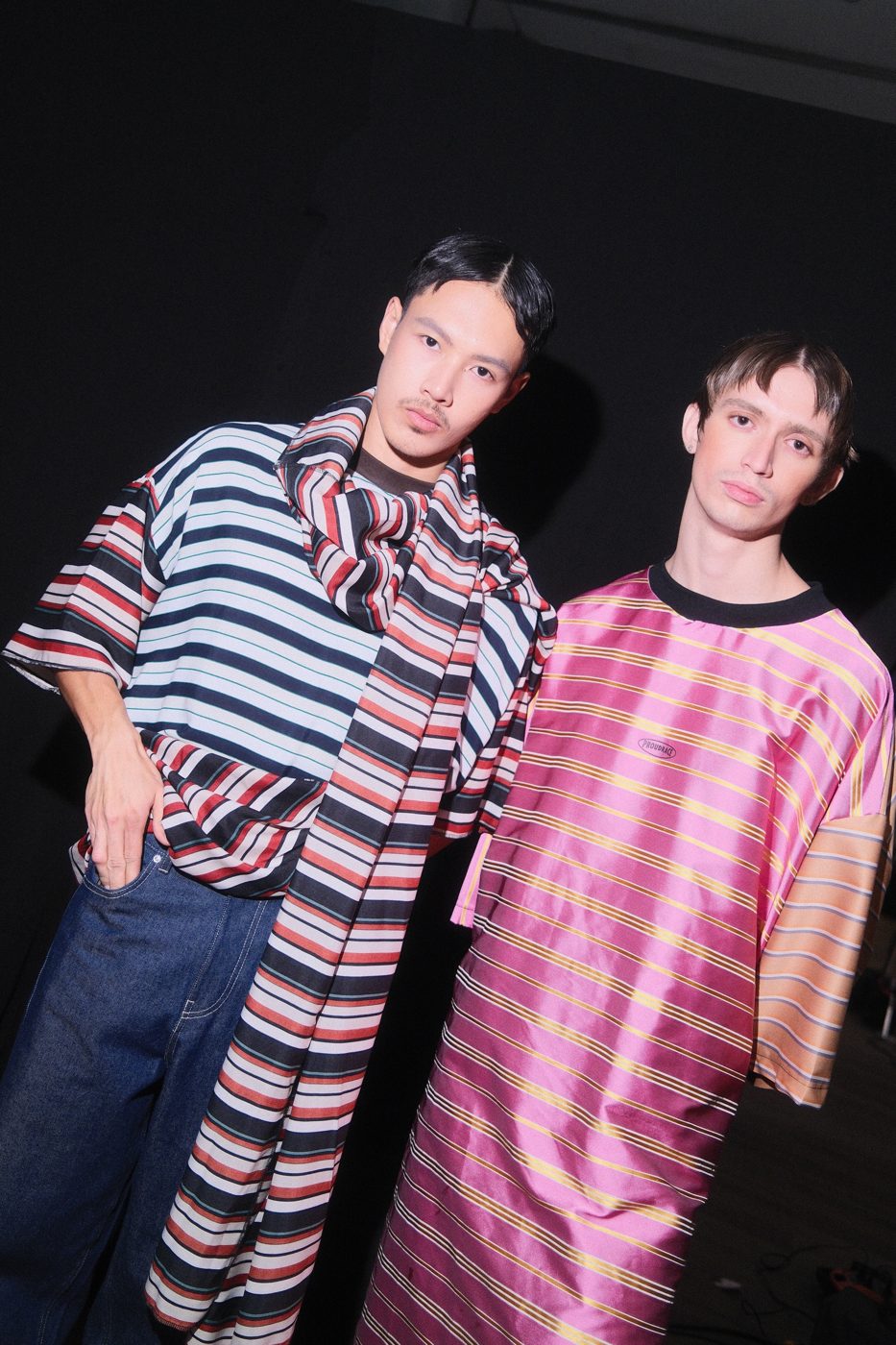 Two models in oversized striped satin, one in shiny pink, under direct flash