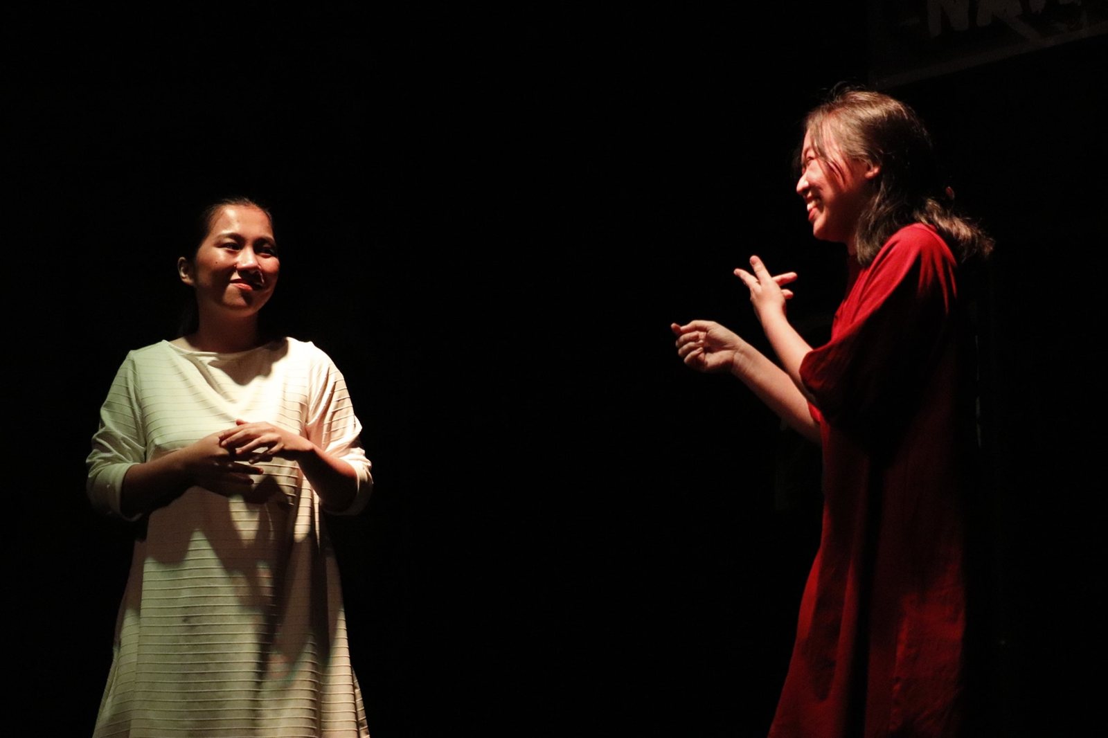 Two actors in white and red facing each other in a pool of light