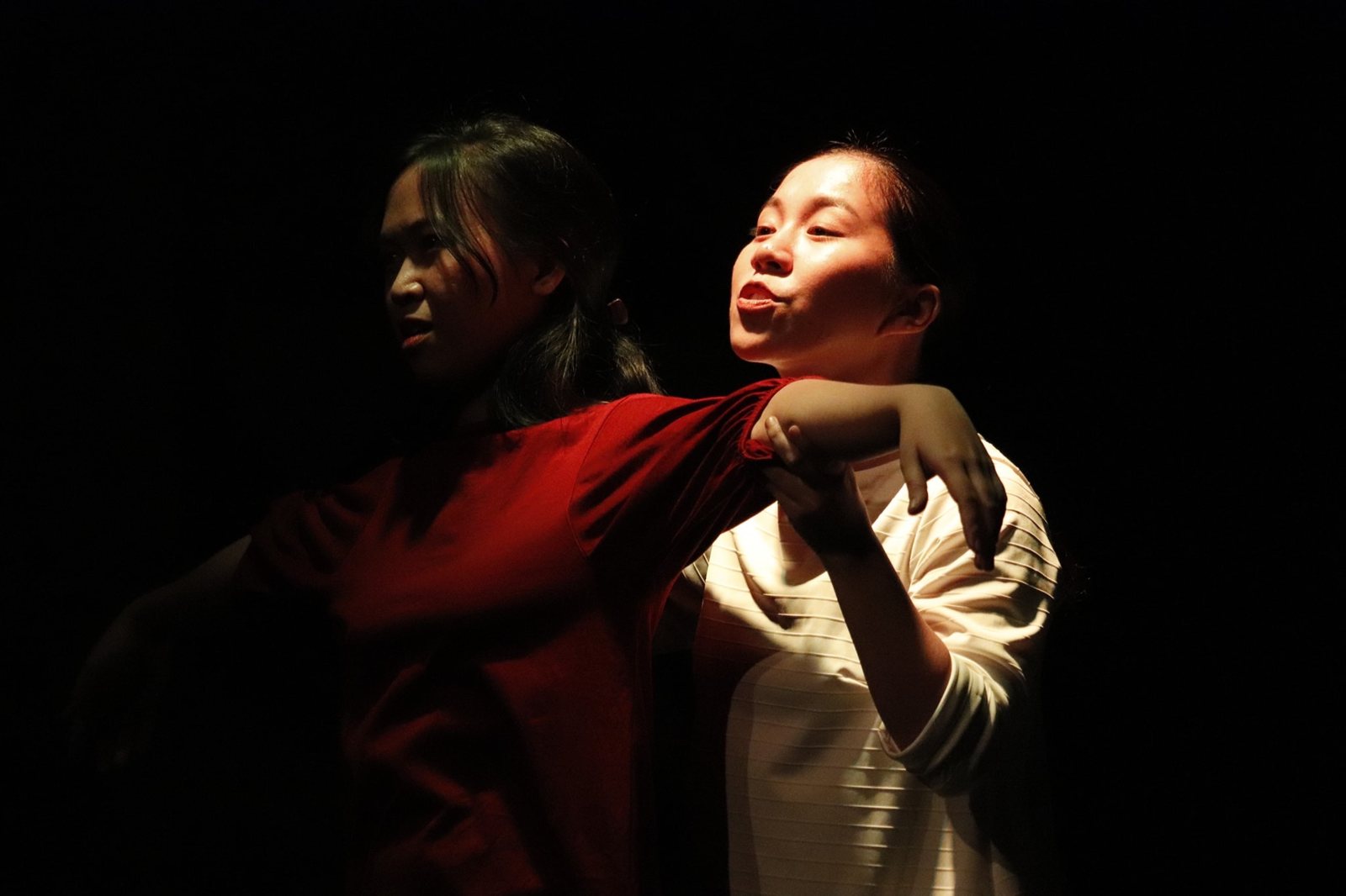 Two actors pressed together in hard side light, one arm draped over the other