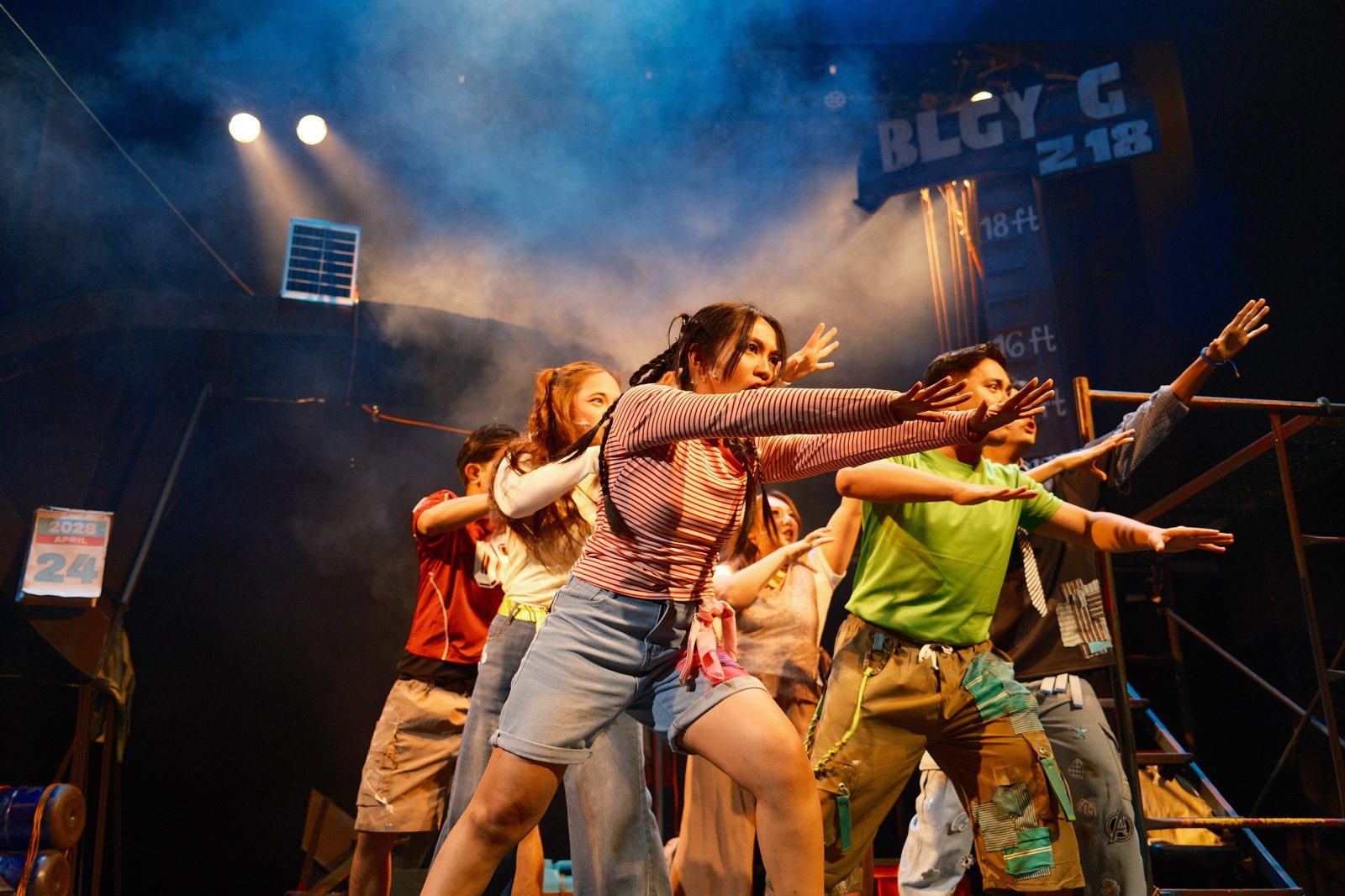 The ensemble lunging forward with arms outstretched through blue stage haze