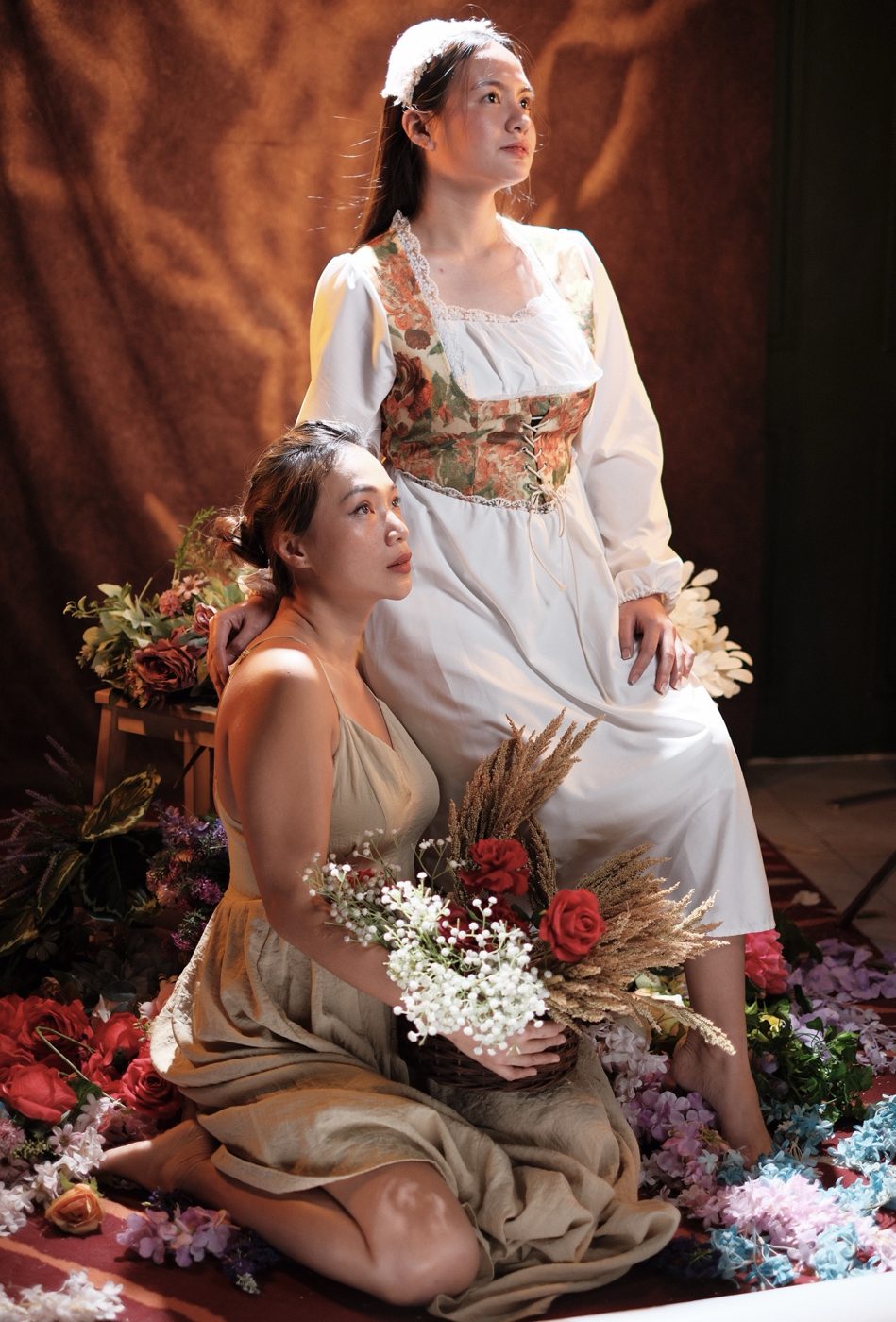 Two women posed on a floor of flowers in warm side light